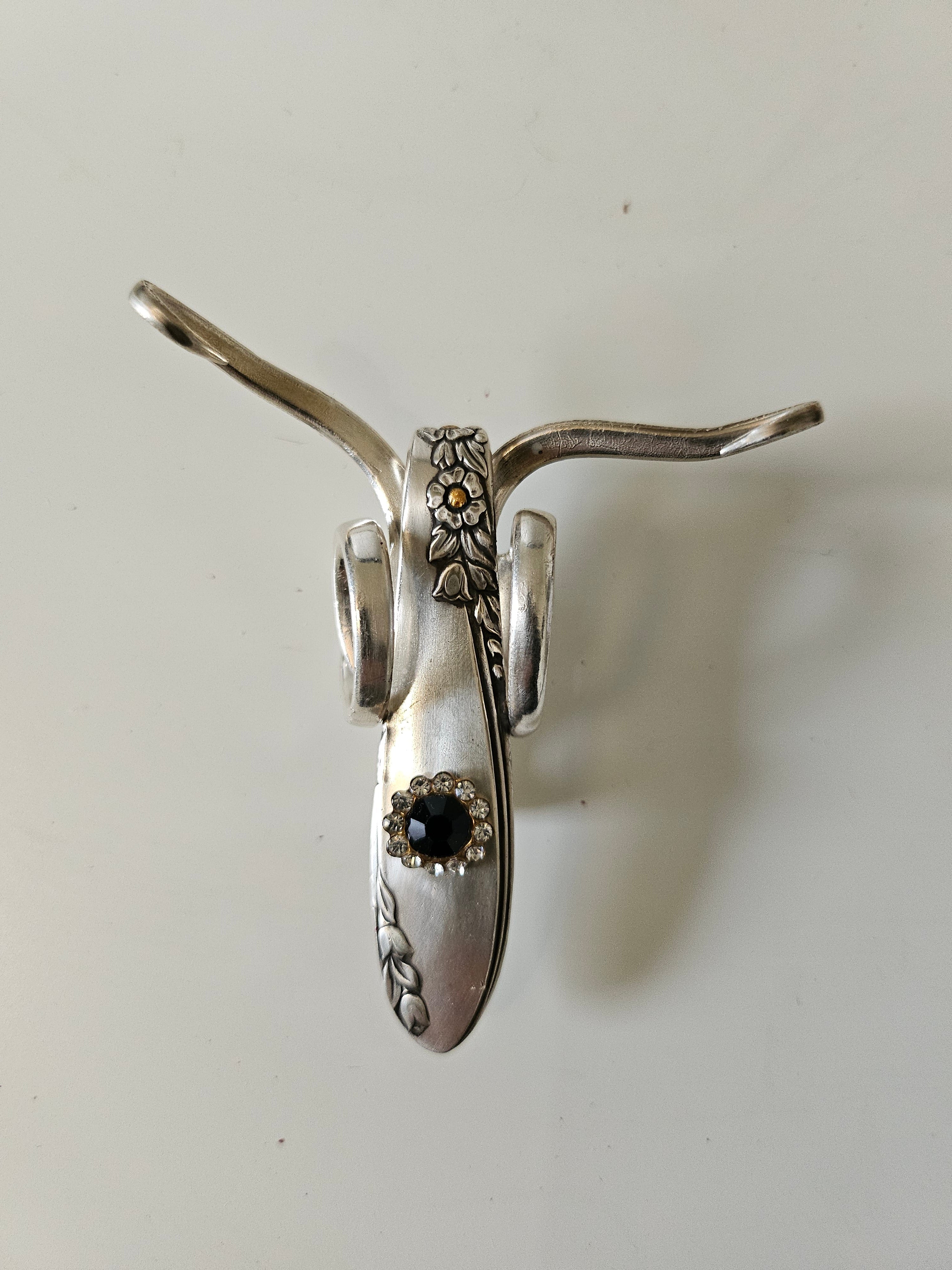 The Jeweled Lucky Fork Cricket is a whimsical, handcrafted sculpture made from repurposed vintage silverware. Each unique piece, shaped from antique forks, captures the charm of crickets—symbols of luck, prosperity, and protection. Adorned with jewels and aged patina, these one-of-a-kind collectibles add artistry, history, and positive energy to any space.