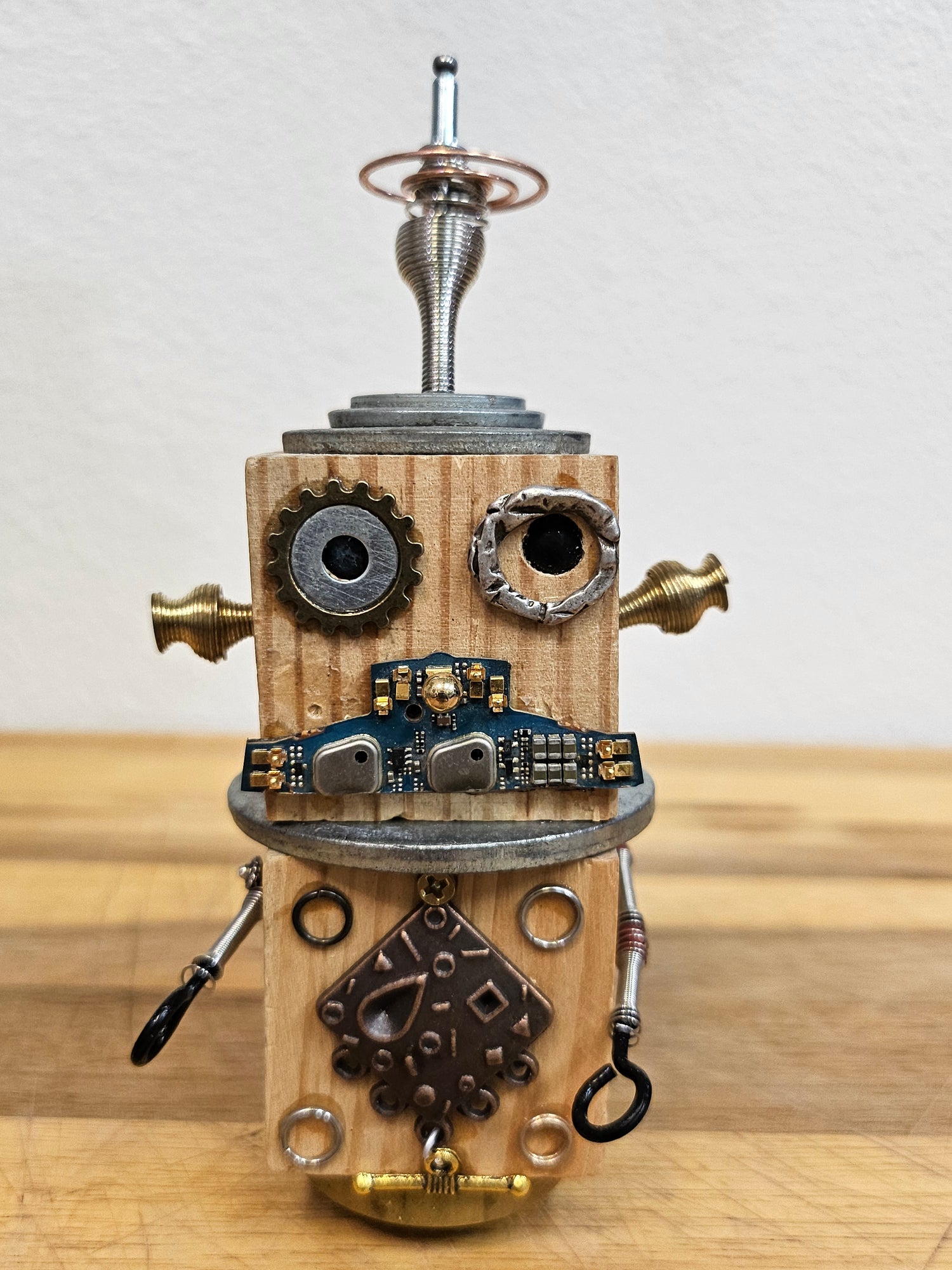 The Handmade Wood Block Steampunk Robot is a unique, decorative figurine crafted from wood with an aged, rustic look. Each robot is one-of-a-kind for display only. Includes a heart-shaped balloon. Available in various sizes, it&