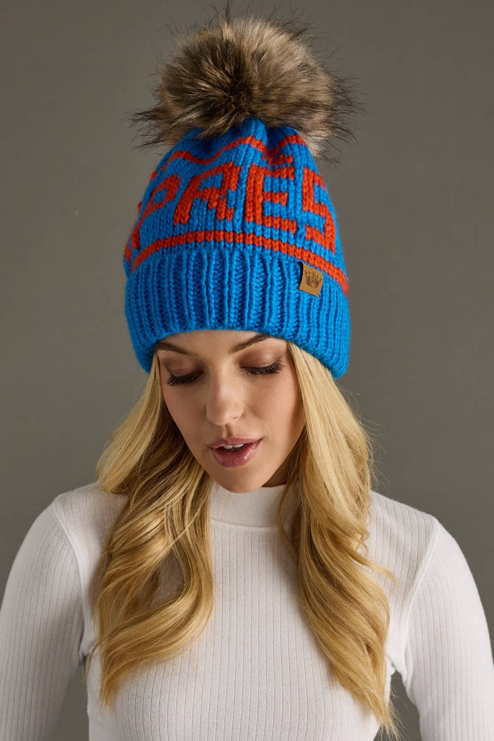 Blue and orange Après knit hat with a natural-toned faux fur pom and cozy fleece lining. Made from 100% acrylic for colorful, comfortable winter style.