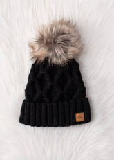 Black diamond cable knit pom hat with natural faux fur pom. Fleece lined for extra warmth and comfort. Classic 100% acrylic design for timeless winter style.