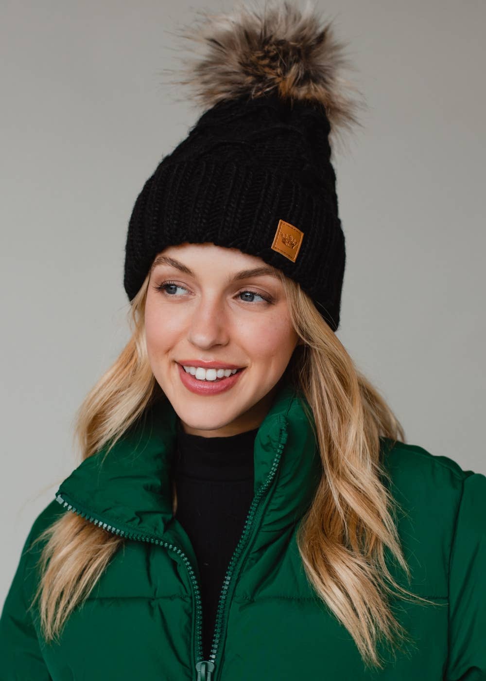 Black diamond cable knit pom hat with natural faux fur pom. Fleece lined for extra warmth and comfort. Classic 100% acrylic design for timeless winter style.