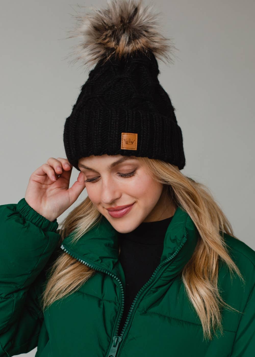 Black diamond cable knit pom hat with natural faux fur pom. Fleece lined for extra warmth and comfort. Classic 100% acrylic design for timeless winter style.