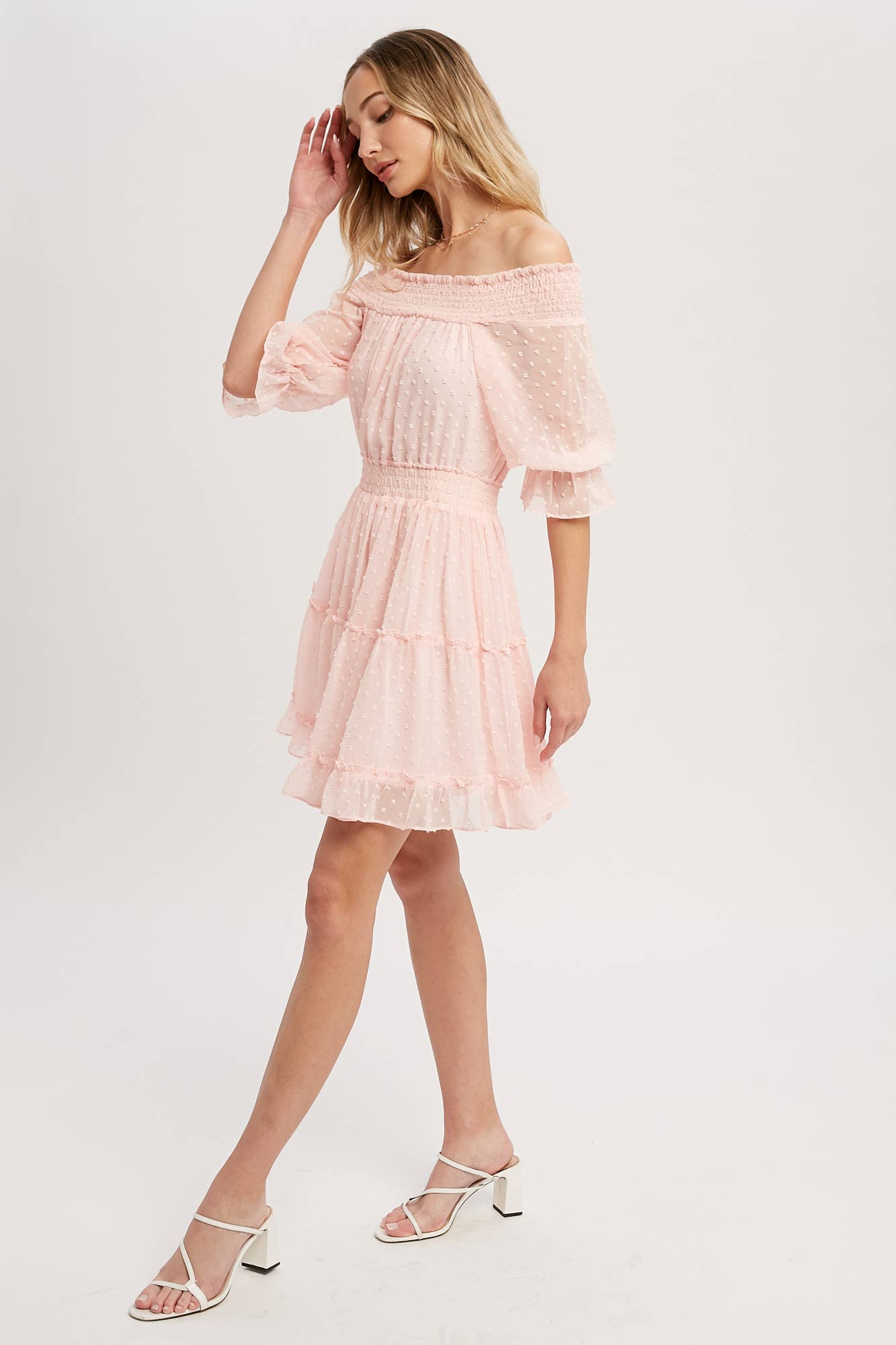 Swiss dot chiffon off-the-shoulder mini dress with elastic waist, bell sleeves, and tiered ruffle hem. Soft blush, relaxed fit, feminine silhouette.