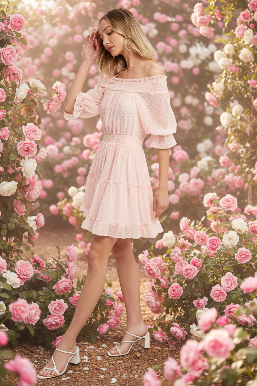 Swiss dot chiffon off-the-shoulder mini dress with elastic waist, bell sleeves, and tiered ruffle hem. Soft blush, relaxed fit, feminine silhouette.