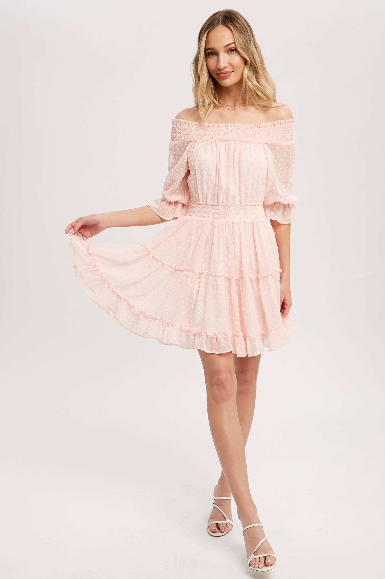 Swiss dot chiffon off-the-shoulder mini dress with elastic waist, bell sleeves, and tiered ruffle hem. Soft blush, relaxed fit, feminine silhouette.