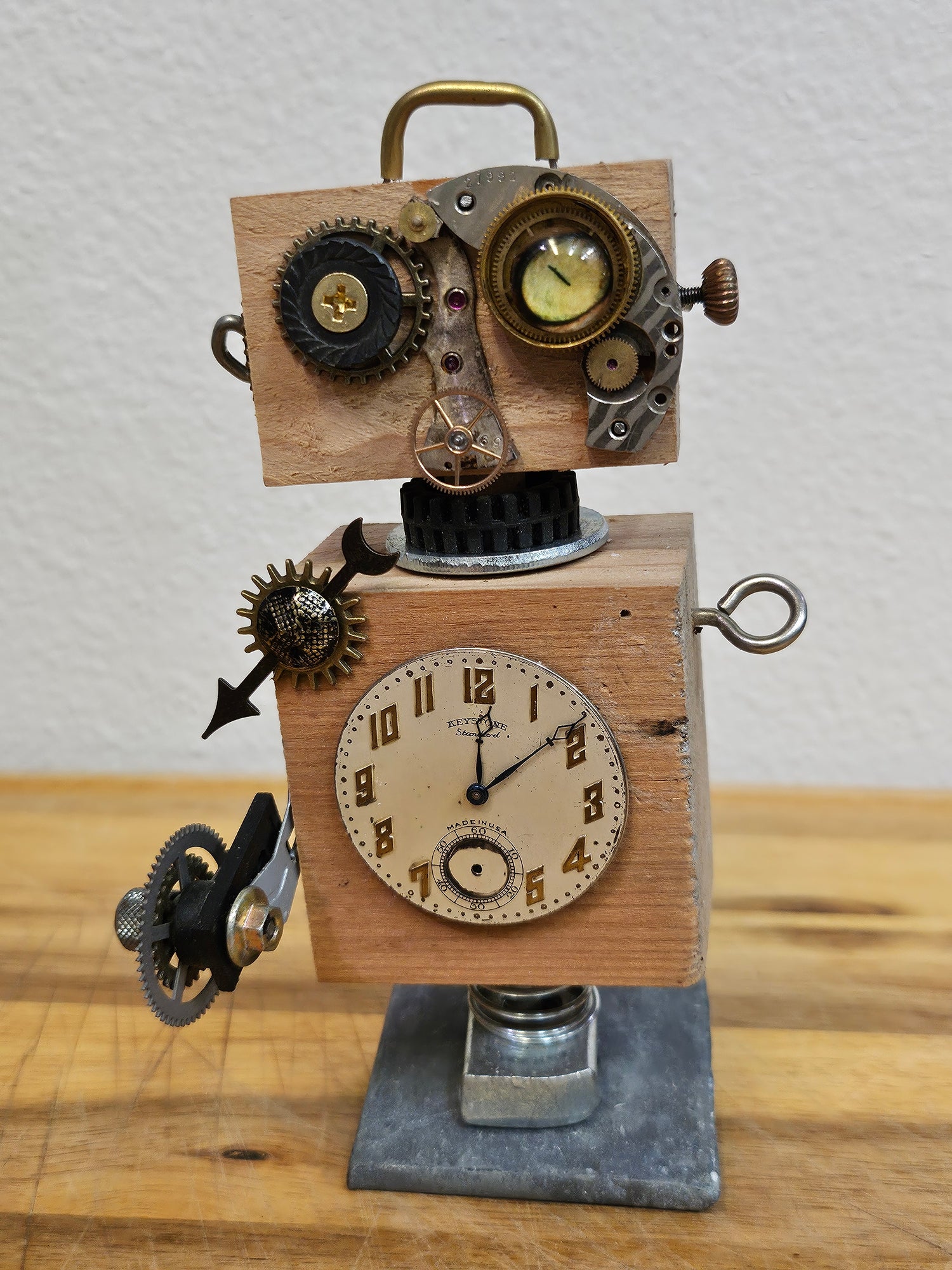 The Handmade Wood Block Steampunk Robot is a unique, decorative figurine crafted from wood with an aged, rustic look. Each robot is one-of-a-kind for display only. Includes a heart-shaped balloon. Available in various sizes, it&