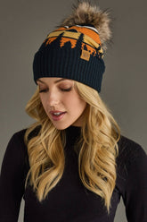 Dark navy knit hat with forest landscape design & natural faux fur pom. Warm, stretchy, and stylish—crafted from 85% acrylic & 15% spandex for comfort.
