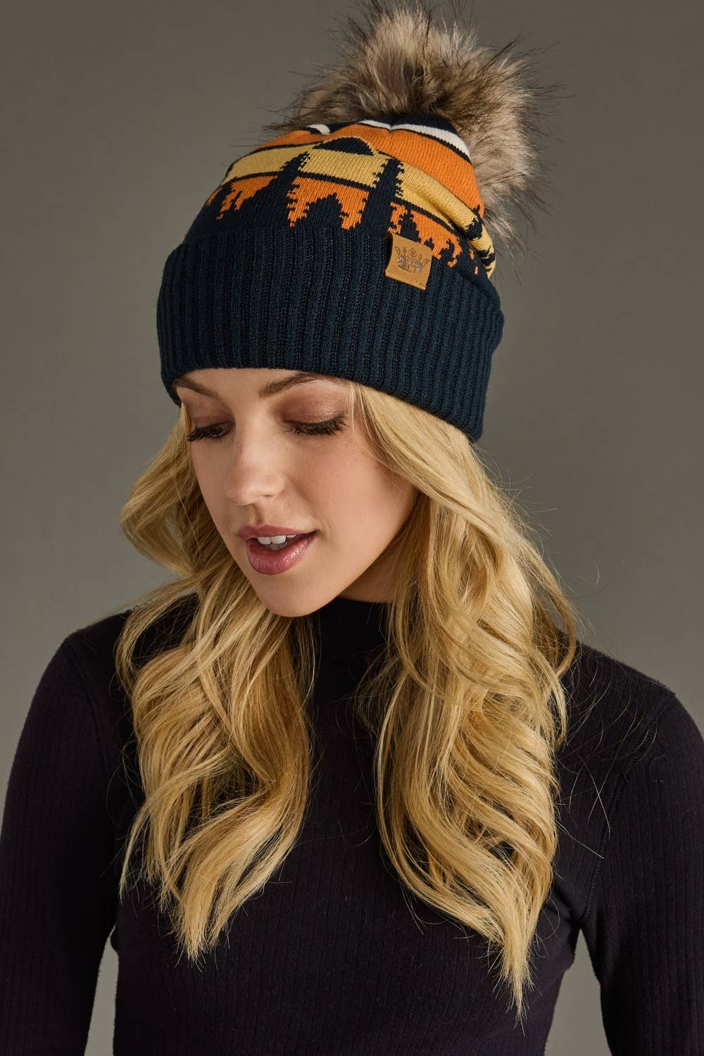 Dark navy knit hat with forest landscape design & natural faux fur pom. Warm, stretchy, and stylish—crafted from 85% acrylic & 15% spandex for comfort.