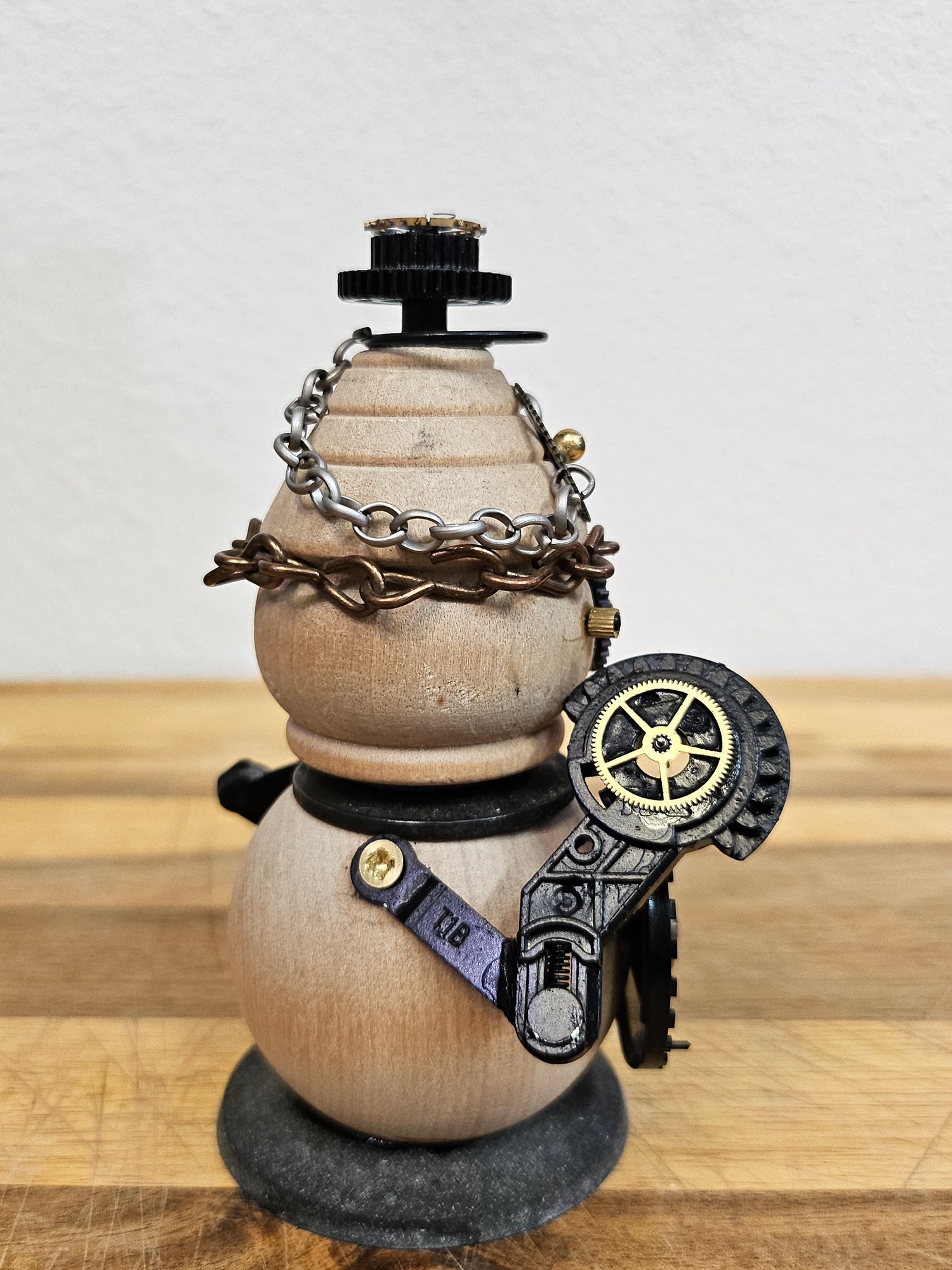 The Handmade Wood Block Steampunk Robot is a unique, decorative figurine crafted from wood with an aged, rustic look. Each robot is one-of-a-kind for display only. Includes a heart-shaped balloon. Available in various sizes, it&