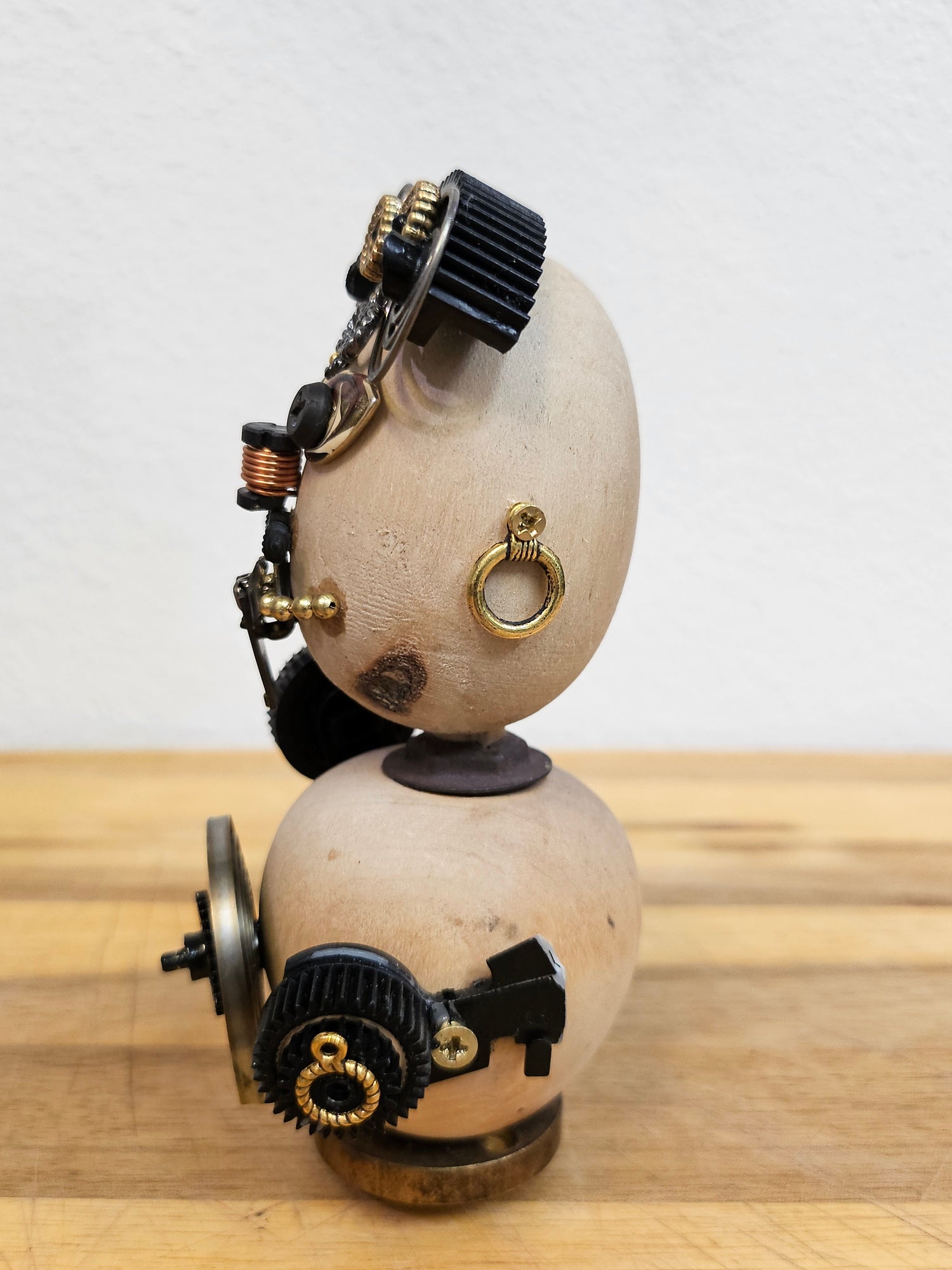 The Handmade Wood Block Steampunk Robot is a unique, decorative figurine crafted from wood with an aged, rustic look. Each robot is one-of-a-kind for display only. Includes a heart-shaped balloon. Available in various sizes, it&
