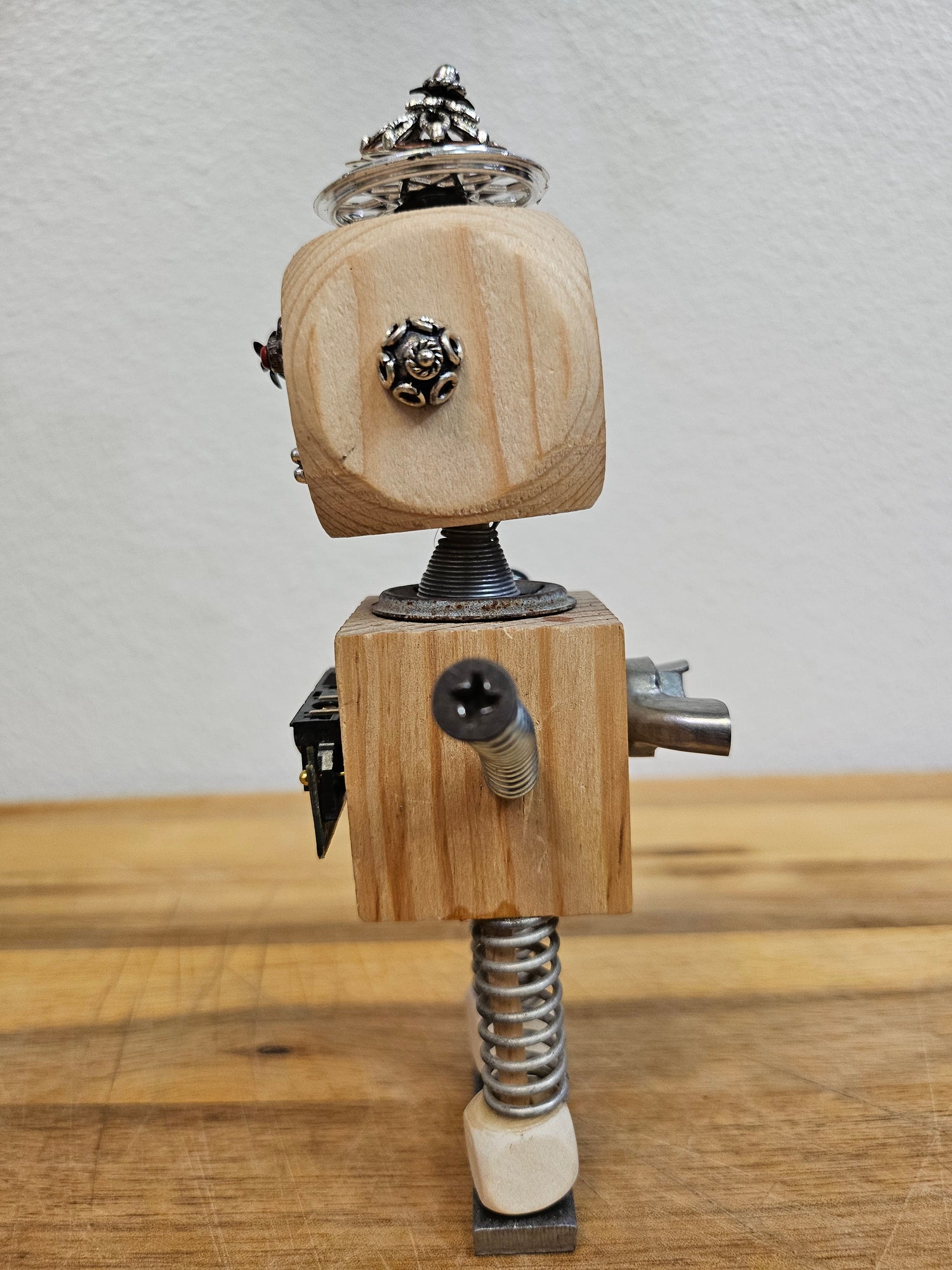 The Handmade Wood Block Steampunk Robot is a unique, decorative figurine crafted from wood with an aged, rustic look. Each robot is one-of-a-kind for display only. Includes a heart-shaped balloon. Available in various sizes, it&