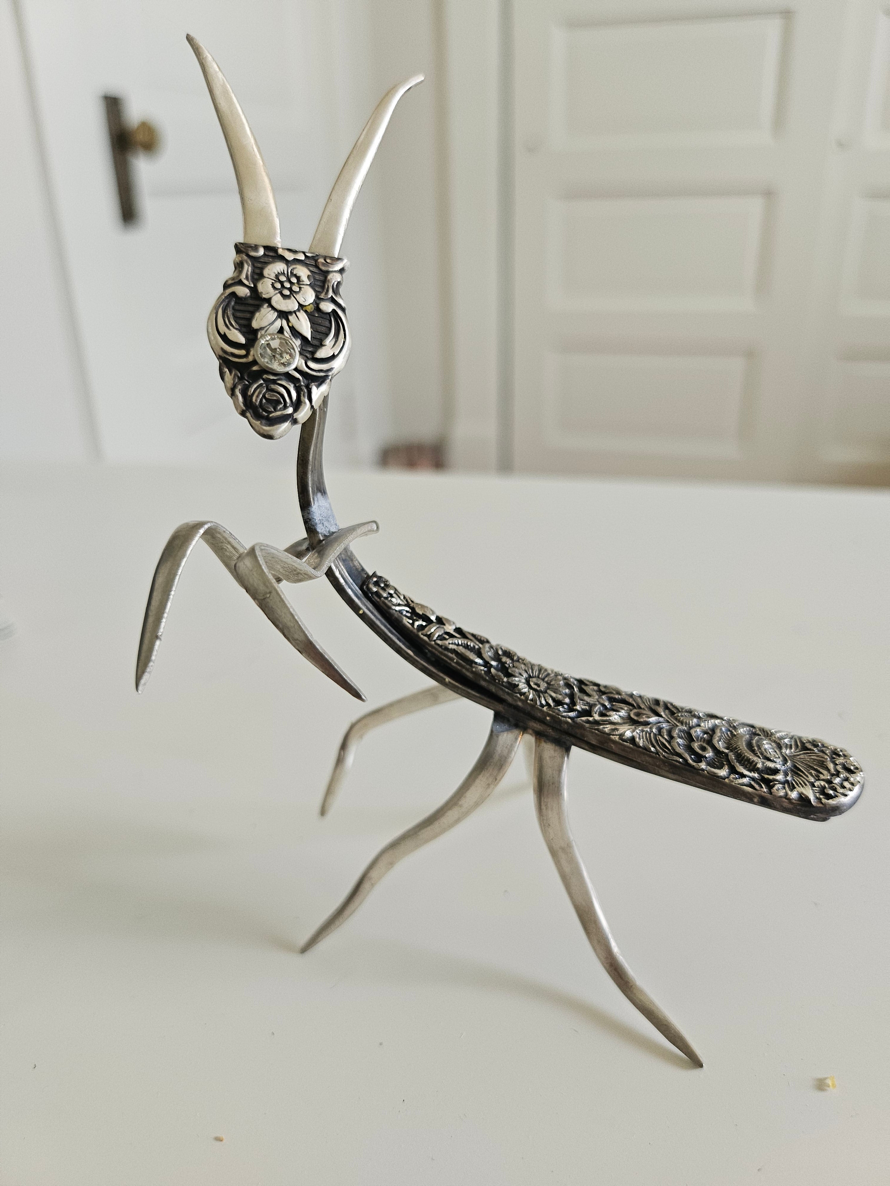 Handcrafted 5" x 4" praying mantis sculpture made from vintage silverware. Unique, whimsical art with gemstone accents and aged patina for mindful décor.
