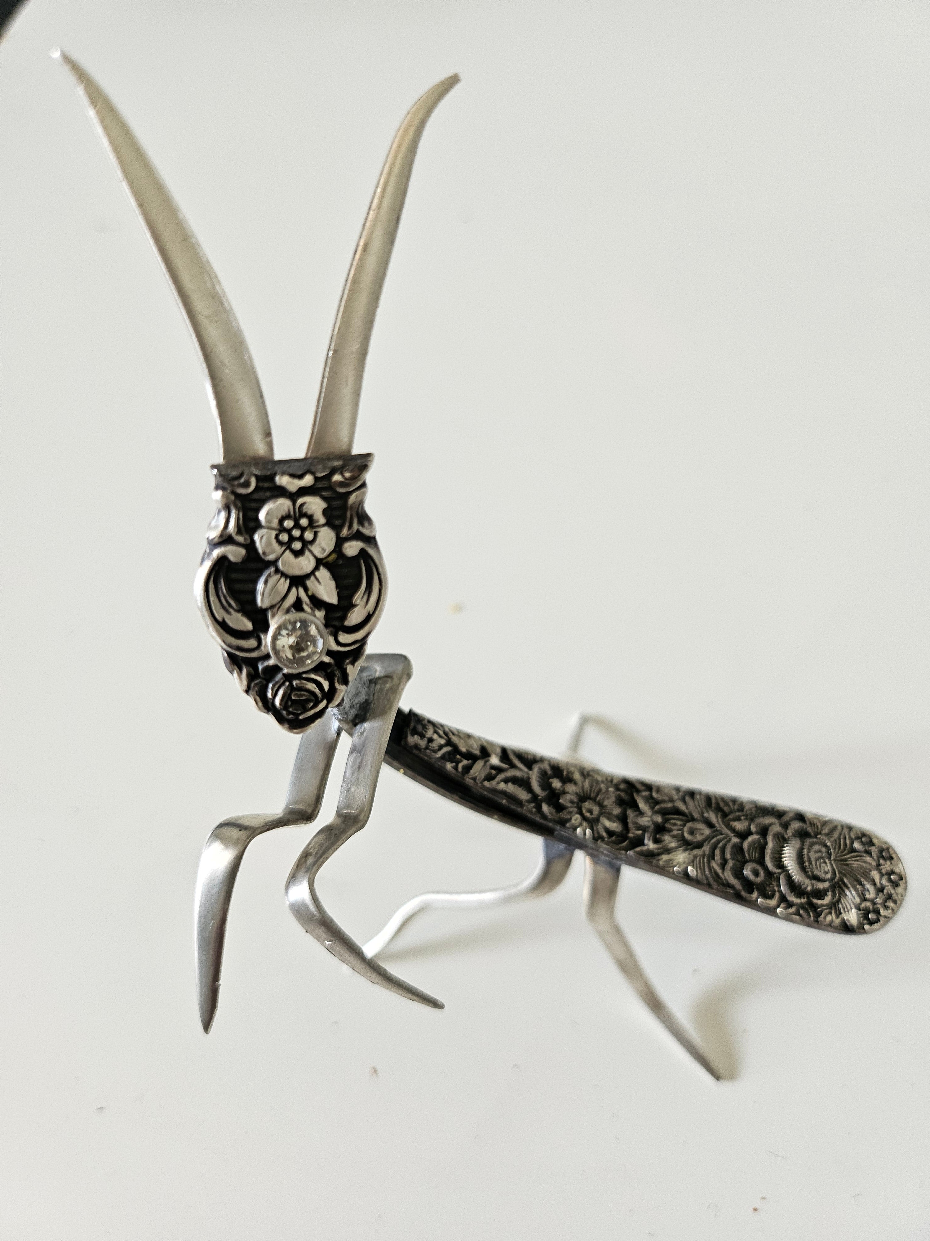 Handcrafted 5" x 4" praying mantis sculpture made from vintage silverware. Unique, whimsical art with gemstone accents and aged patina for mindful décor.