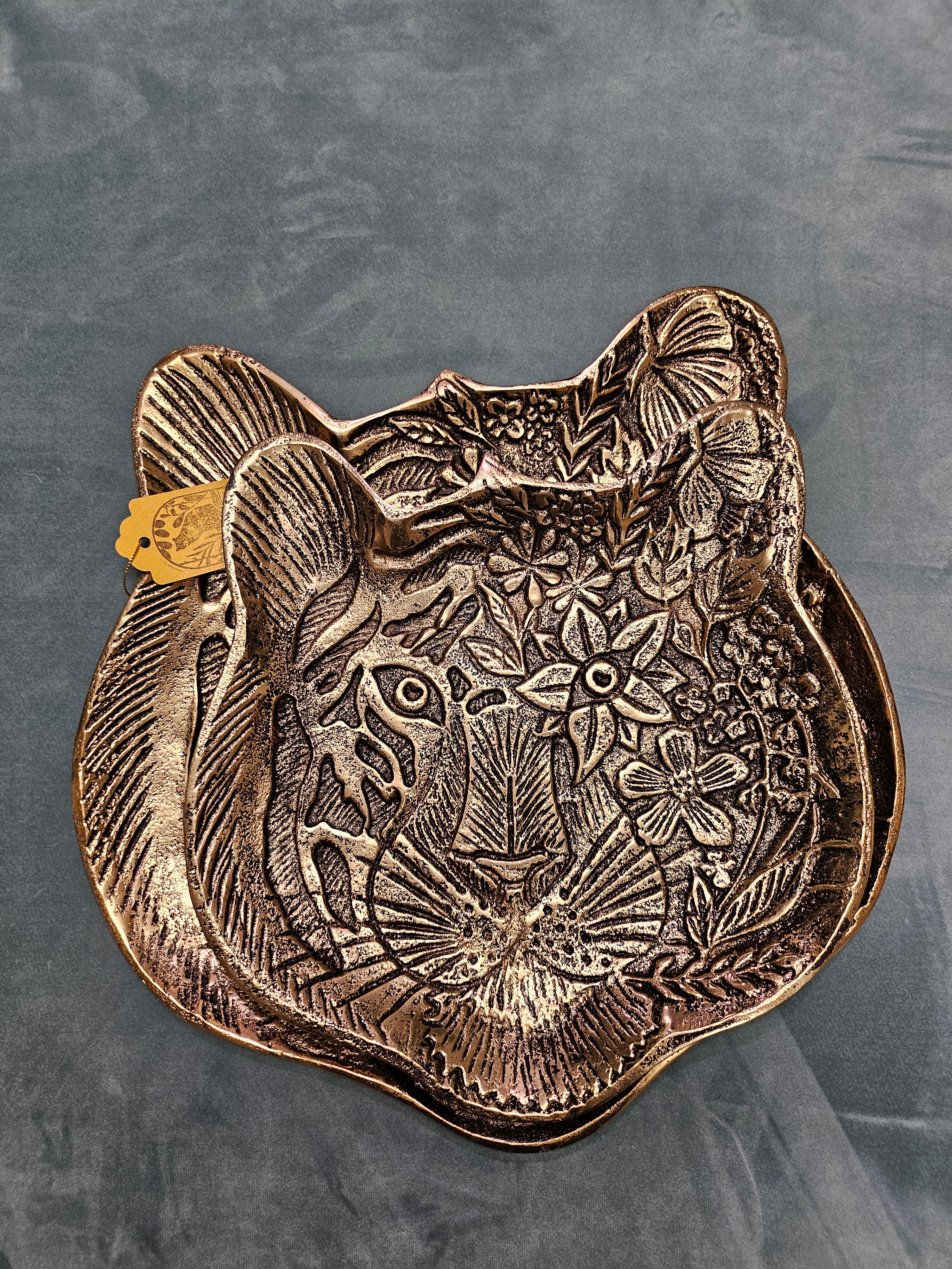 The Tiger Embossed Metal Tray is a luxurious and durable 16 cm x 14.5 cm catchall dish with a golden finish and intricate tiger head design. Perfect for organizing jewelry, keys, or coins, it adds a regal touch to any space. Ideal as a functional decor piece or a thoughtful gift for art and animal lovers