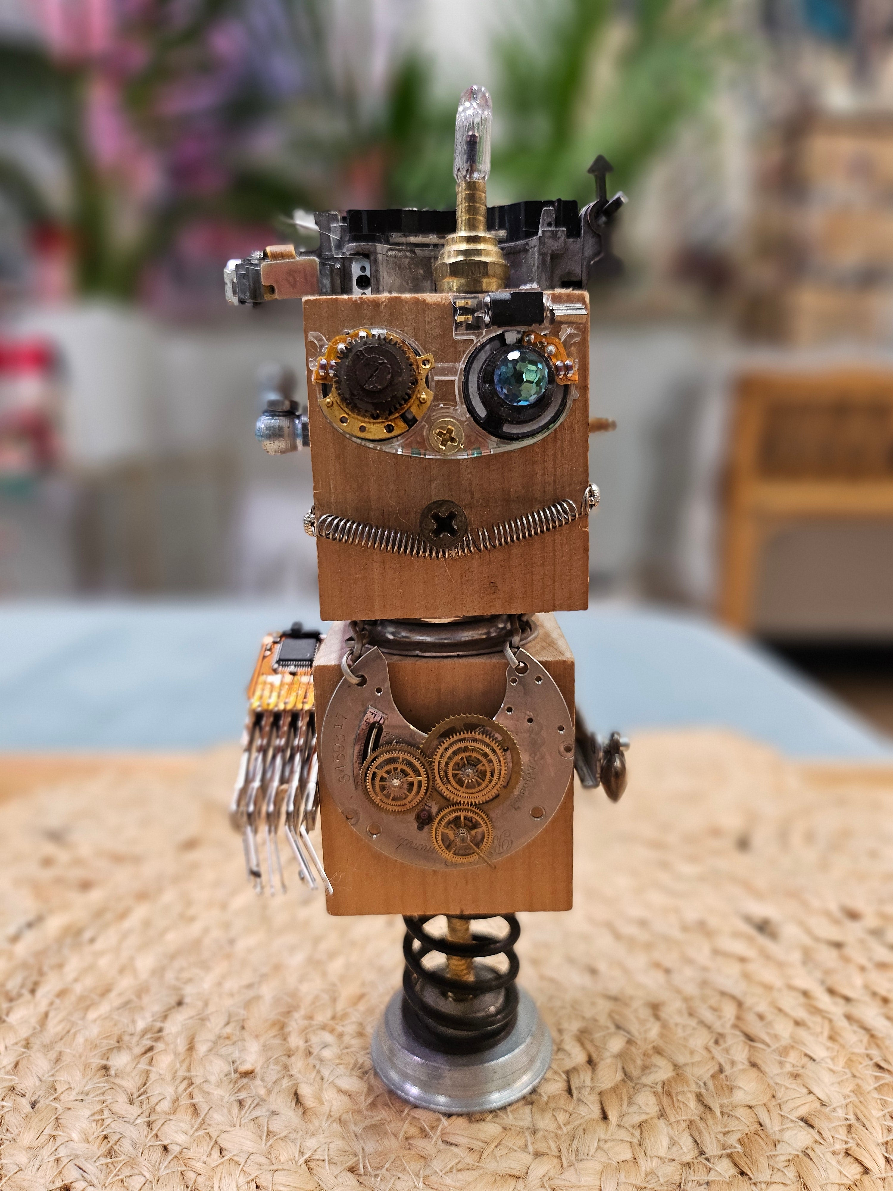 The Handmade Wood Block Steampunk Robot is a unique, decorative figurine crafted from wood with an aged, rustic look. Each robot is one-of-a-kind for display only. Includes a heart-shaped balloon. Available in various sizes, it&
