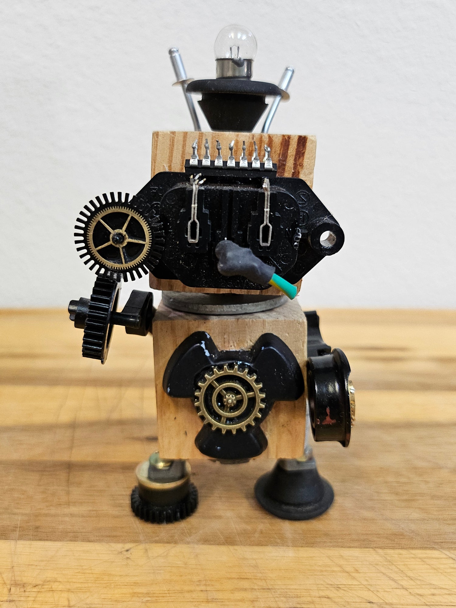 The Handmade Wood Block Steampunk Robot is a unique, decorative figurine crafted from wood with an aged, rustic look. Each robot is one-of-a-kind for display only. Includes a heart-shaped balloon. Available in various sizes, it&