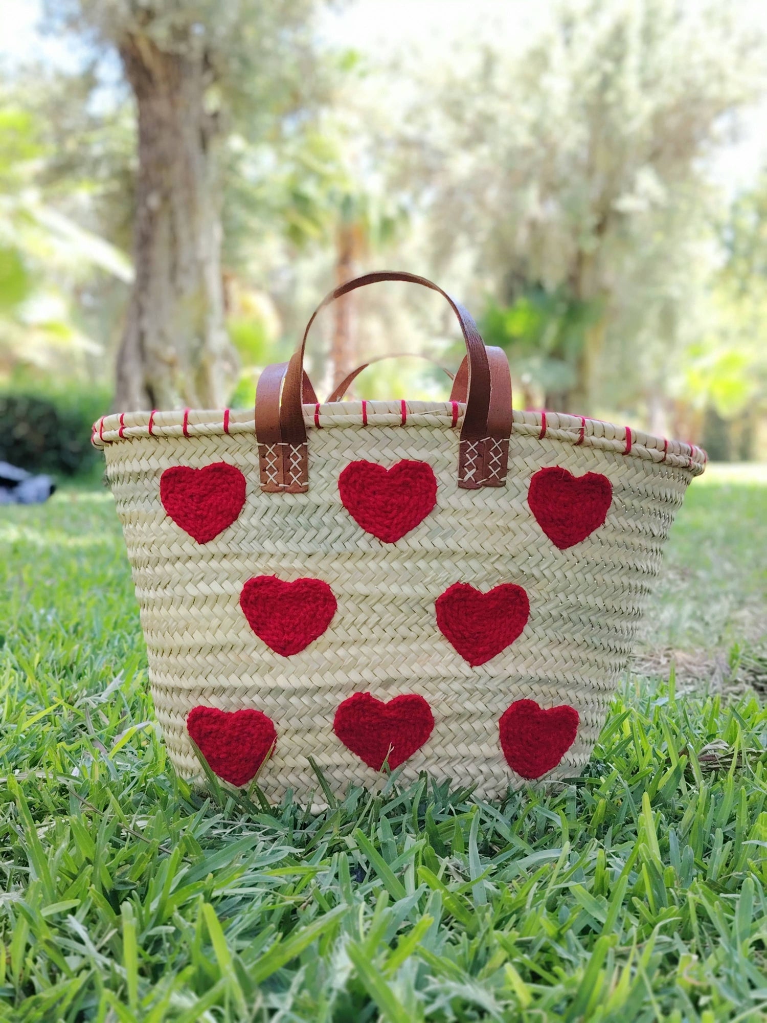 Handwoven straw tote with red crochet hearts and leather handles. Eco-friendly, artisan-made, and perfect for markets, gifting, or seasonal outings.