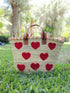 Handwoven straw tote with red crochet hearts and leather handles. Eco-friendly, artisan-made, and perfect for markets, gifting, or seasonal outings.