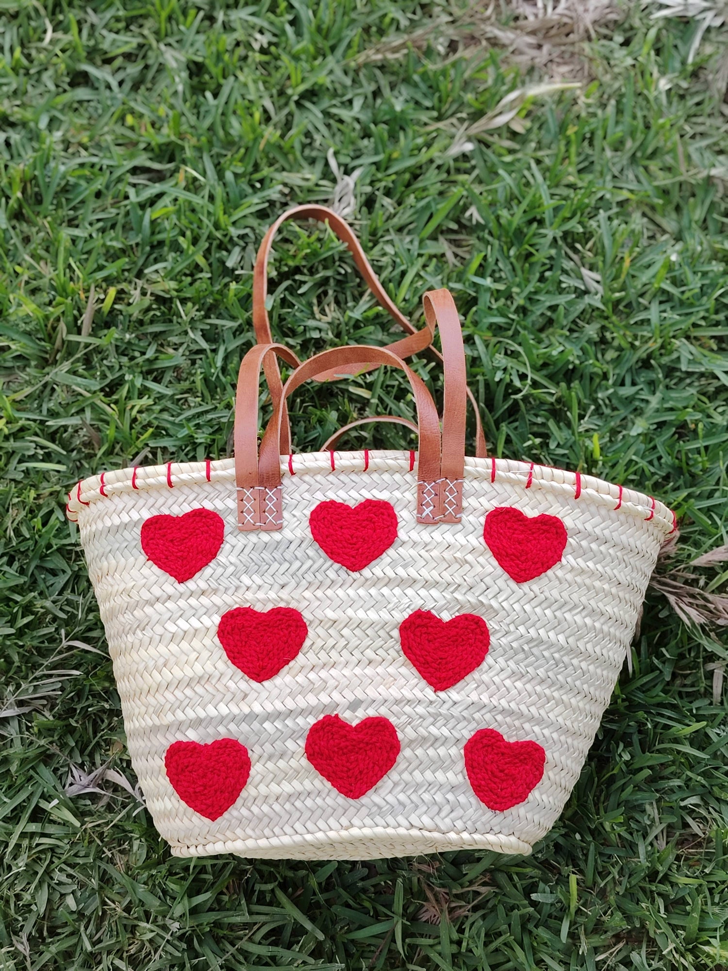 Handwoven straw tote with red crochet hearts and leather handles. Eco-friendly, artisan-made, and perfect for markets, gifting, or seasonal outings.
