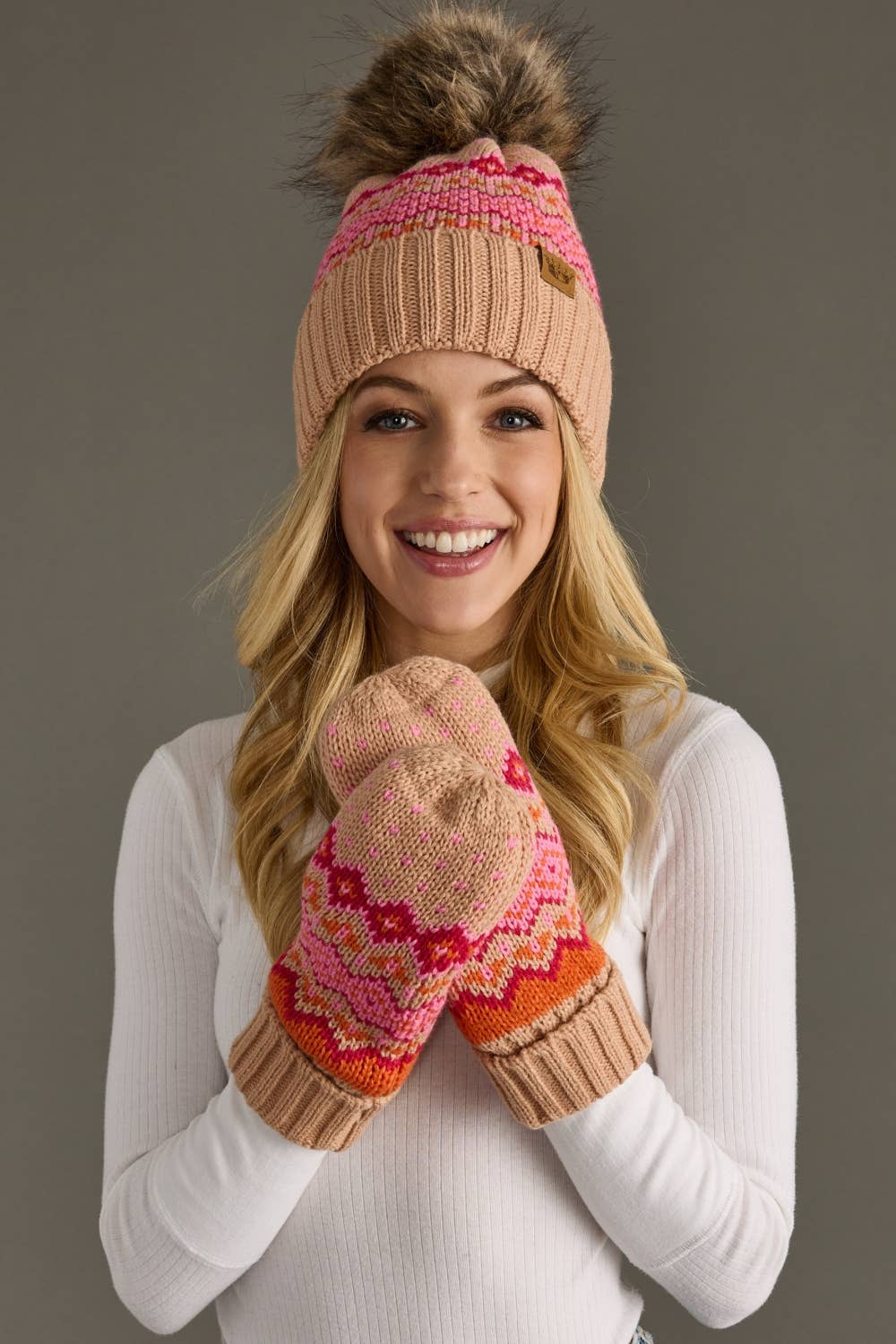 Blush, pink & orange patterned knit hat with natural faux fur pom. Fleece lined for extra warmth & pairs perfectly with matching mittens. 100% acrylic.