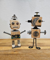 The Handmade Wood Block Steampunk Robot is a unique, decorative figurine crafted from wood with an aged, rustic look. Each robot is one-of-a-kind for display only. Includes a heart-shaped balloon. Available in various sizes, it&