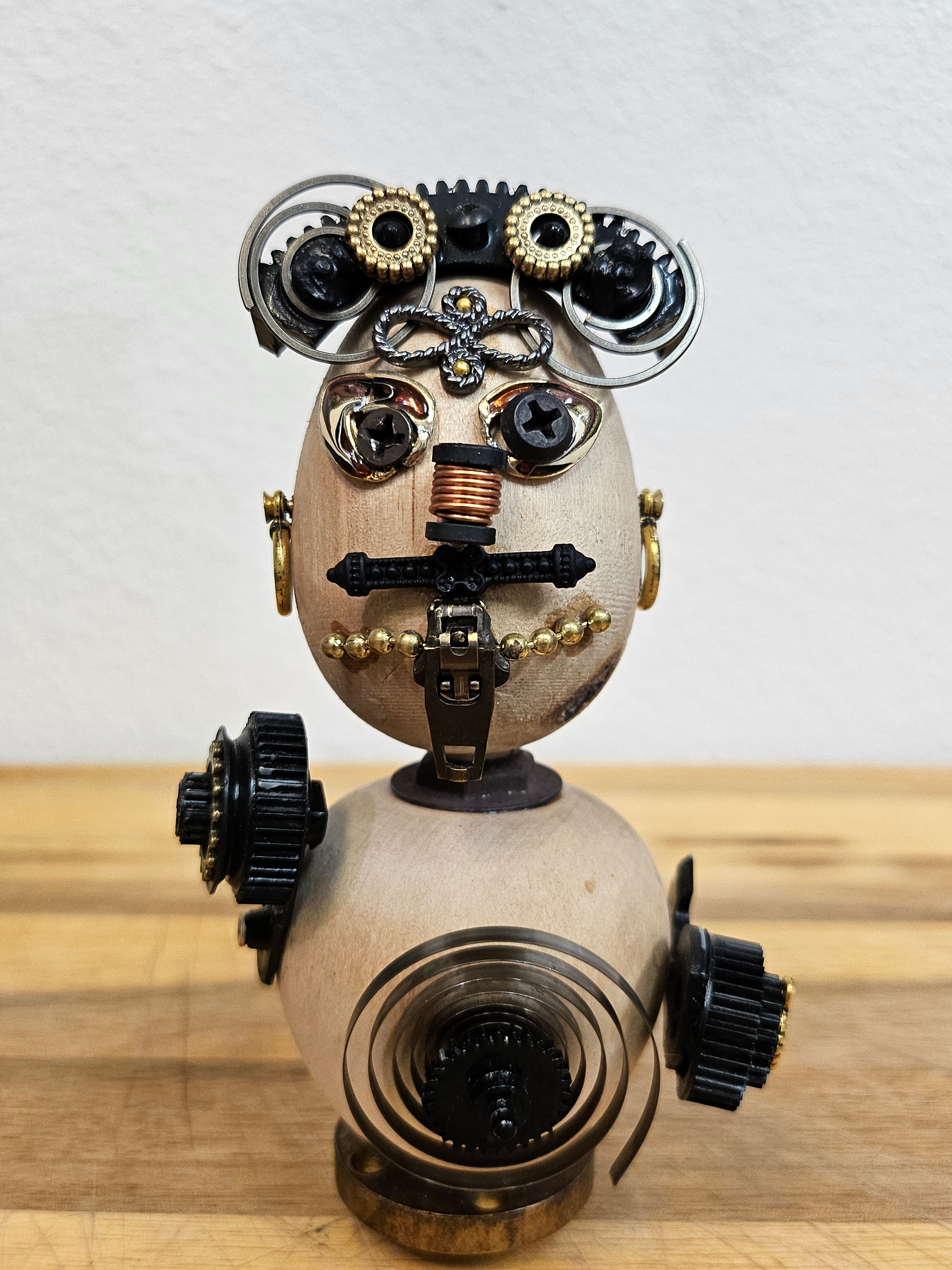 The Handmade Wood Block Steampunk Robot is a unique, decorative figurine crafted from wood with an aged, rustic look. Each robot is one-of-a-kind for display only. Includes a heart-shaped balloon. Available in various sizes, it&