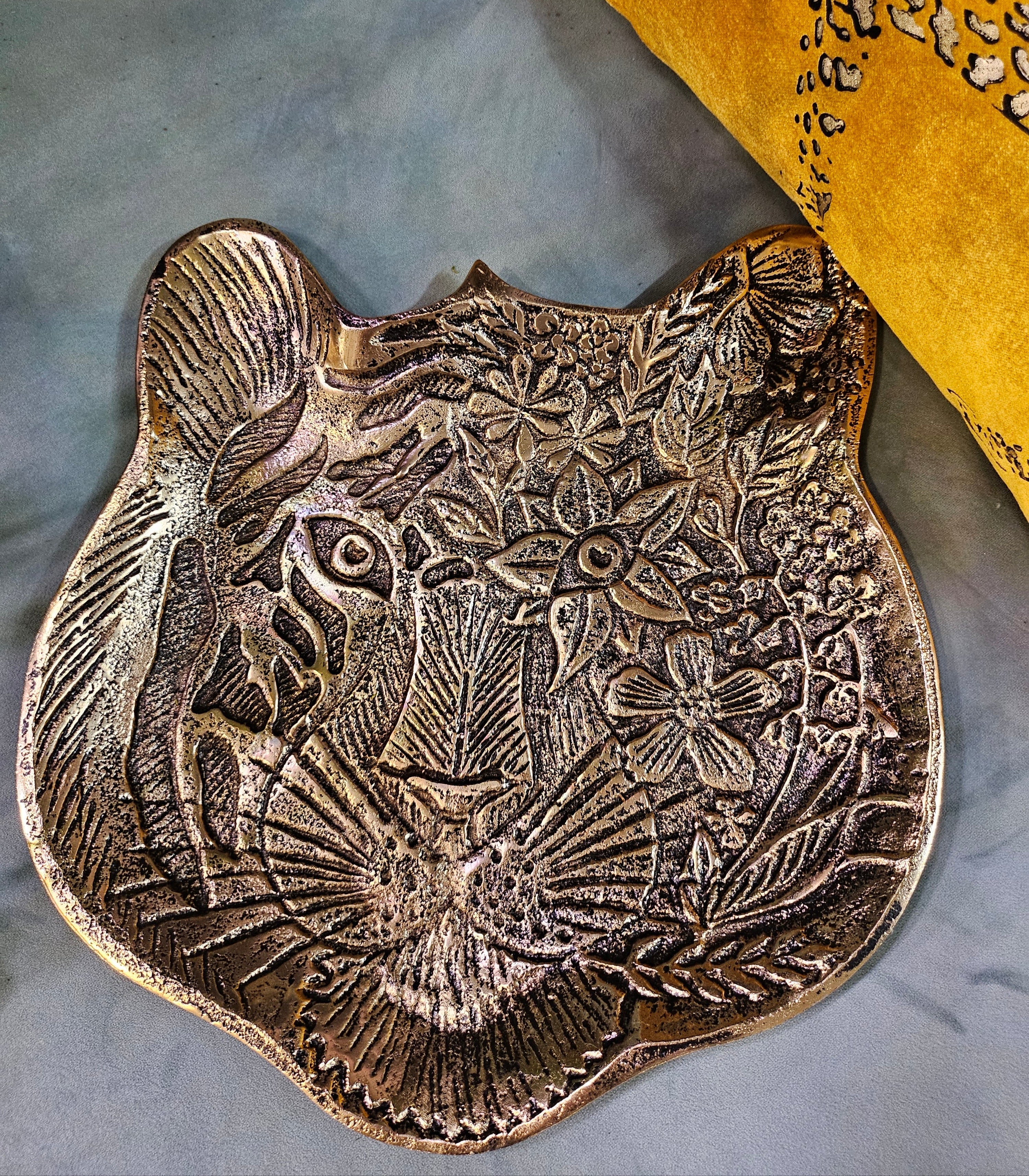 The Tiger Embossed Metal Tray is a luxurious and durable 16 cm x 14.5 cm catchall dish with a golden finish and intricate tiger head design. Perfect for organizing jewelry, keys, or coins, it adds a regal touch to any space. Ideal as a functional decor piece or a thoughtful gift for art and animal lovers.