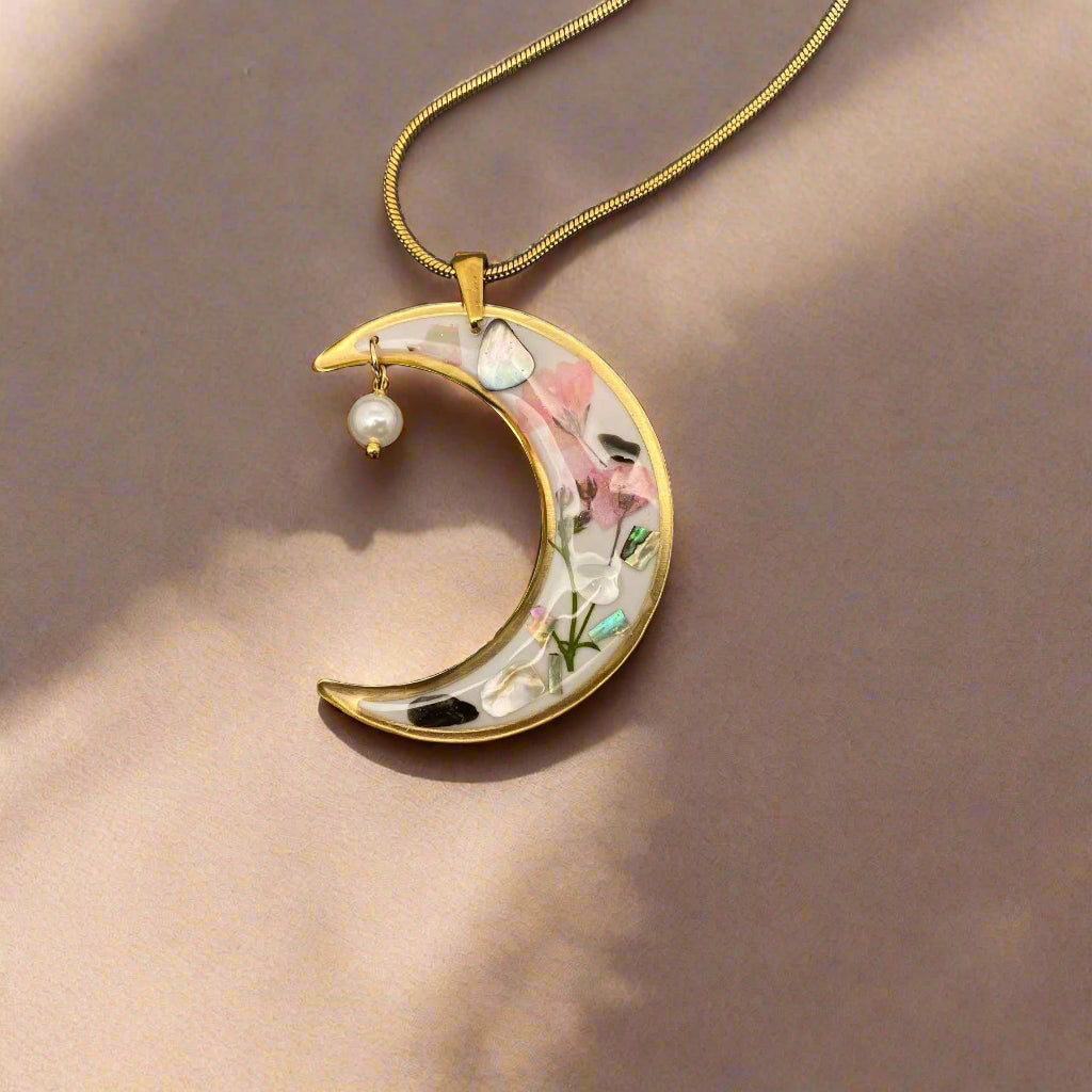 Moon-shaped pendant necklace with real pressed flowers and shell in resin, set in 18K gold-plated brass. Unique, handmade celestial floral jewelry.