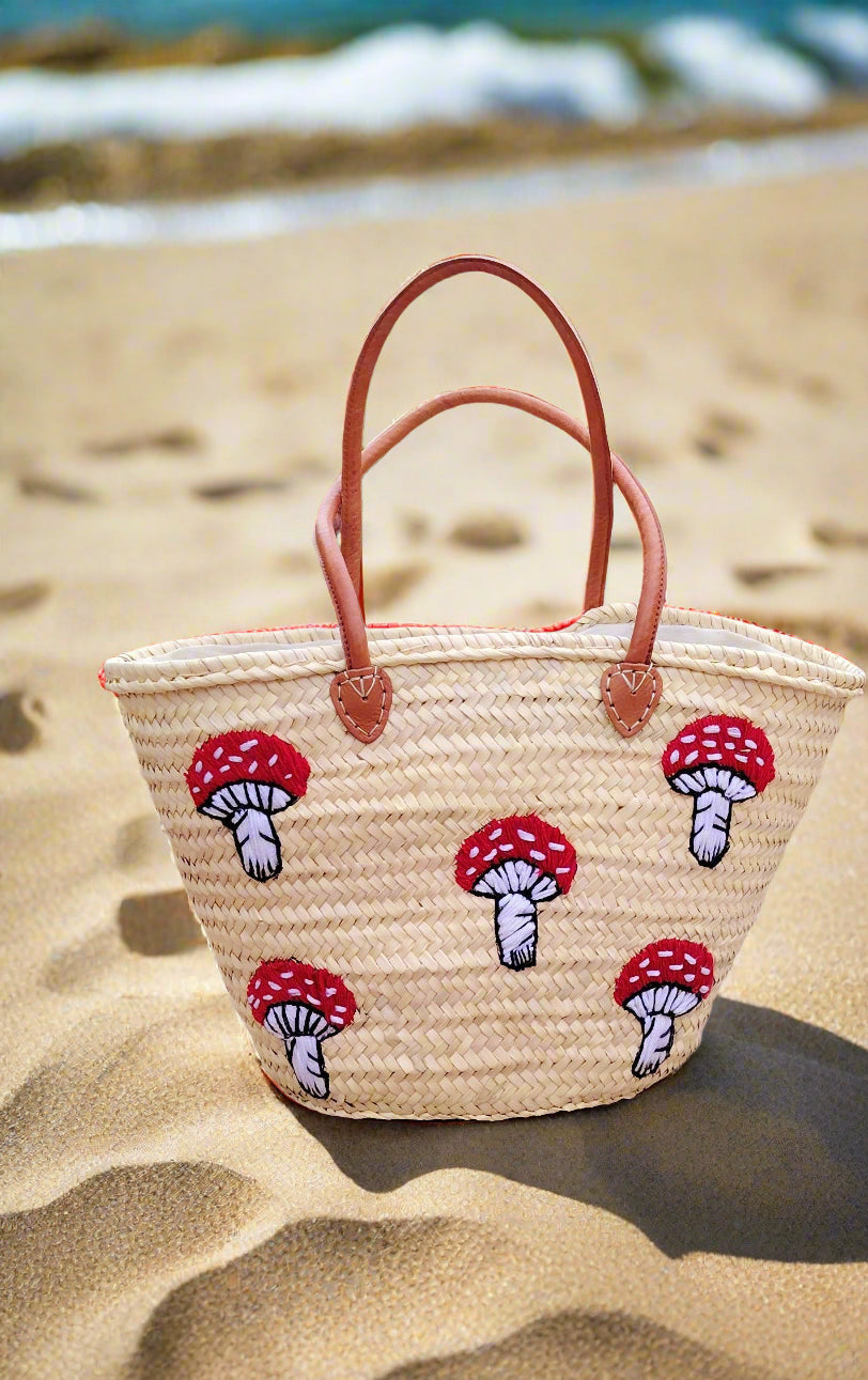 Whimsical straw tote with red mushroom embroidery, leather handles & eco-friendly palm straw. Perfect for market trips, beach days, or unique gifting.