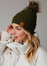 Olive green knit hat with natural faux fur pom. Cozy, stylish, and versatile—crafted from 100% acrylic for warmth and everyday boho-chic winter vibes.
