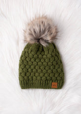 Olive green knit hat with natural faux fur pom. Cozy, stylish, and versatile—crafted from 100% acrylic for warmth and everyday boho-chic winter vibes.
