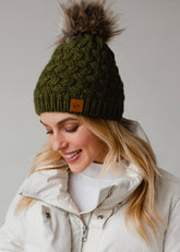 Olive green knit hat with natural faux fur pom. Cozy, stylish, and versatile—crafted from 100% acrylic for warmth and everyday boho-chic winter vibes.