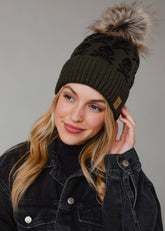 Olive skull pattern knit hat with natural faux fur pom. Fleece lined for cozy warmth and style. 100% acrylic and pairs perfectly with matching mittens.