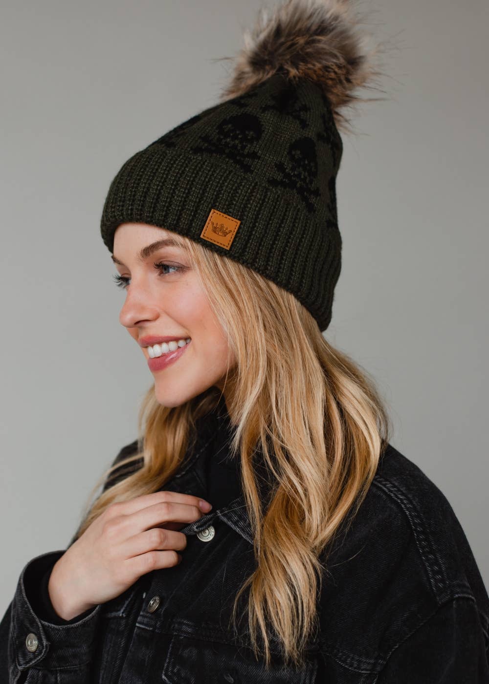 Olive skull pattern knit hat with natural faux fur pom. Fleece lined for cozy warmth and style. 100% acrylic and pairs perfectly with matching mittens.