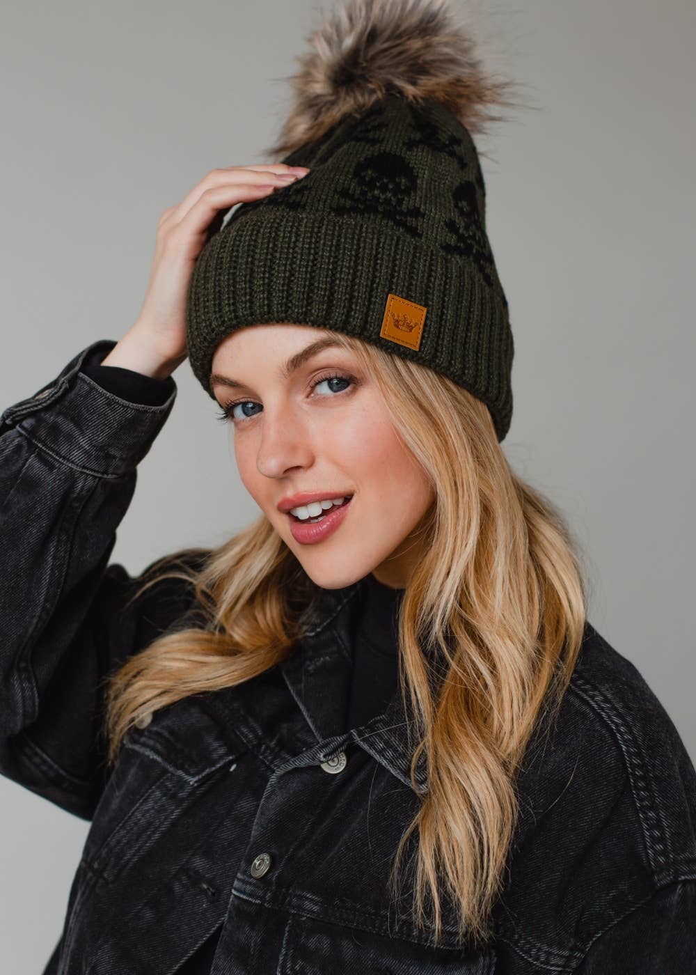 Olive skull pattern knit hat with natural faux fur pom. Fleece lined for cozy warmth and style. 100% acrylic and pairs perfectly with matching mittens.