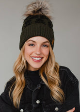 Olive skull pattern knit hat with natural faux fur pom. Fleece lined for cozy warmth and style. 100% acrylic and pairs perfectly with matching mittens.