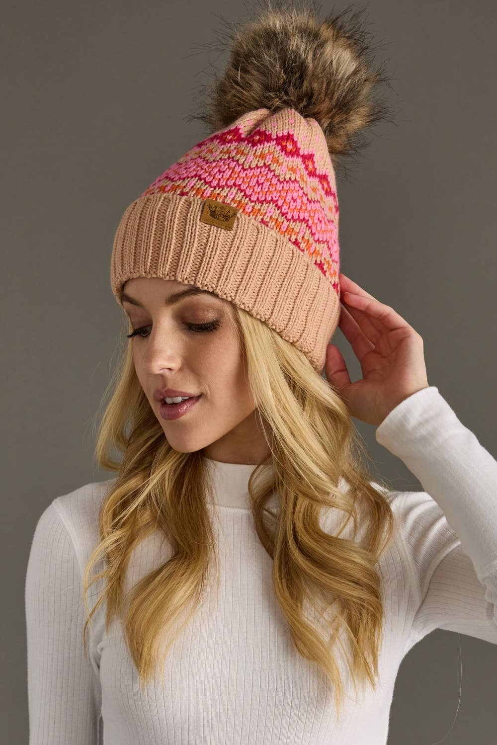 Blush, pink & orange patterned knit hat with natural faux fur pom. Fleece lined for extra warmth & pairs perfectly with matching mittens. 100% acrylic.