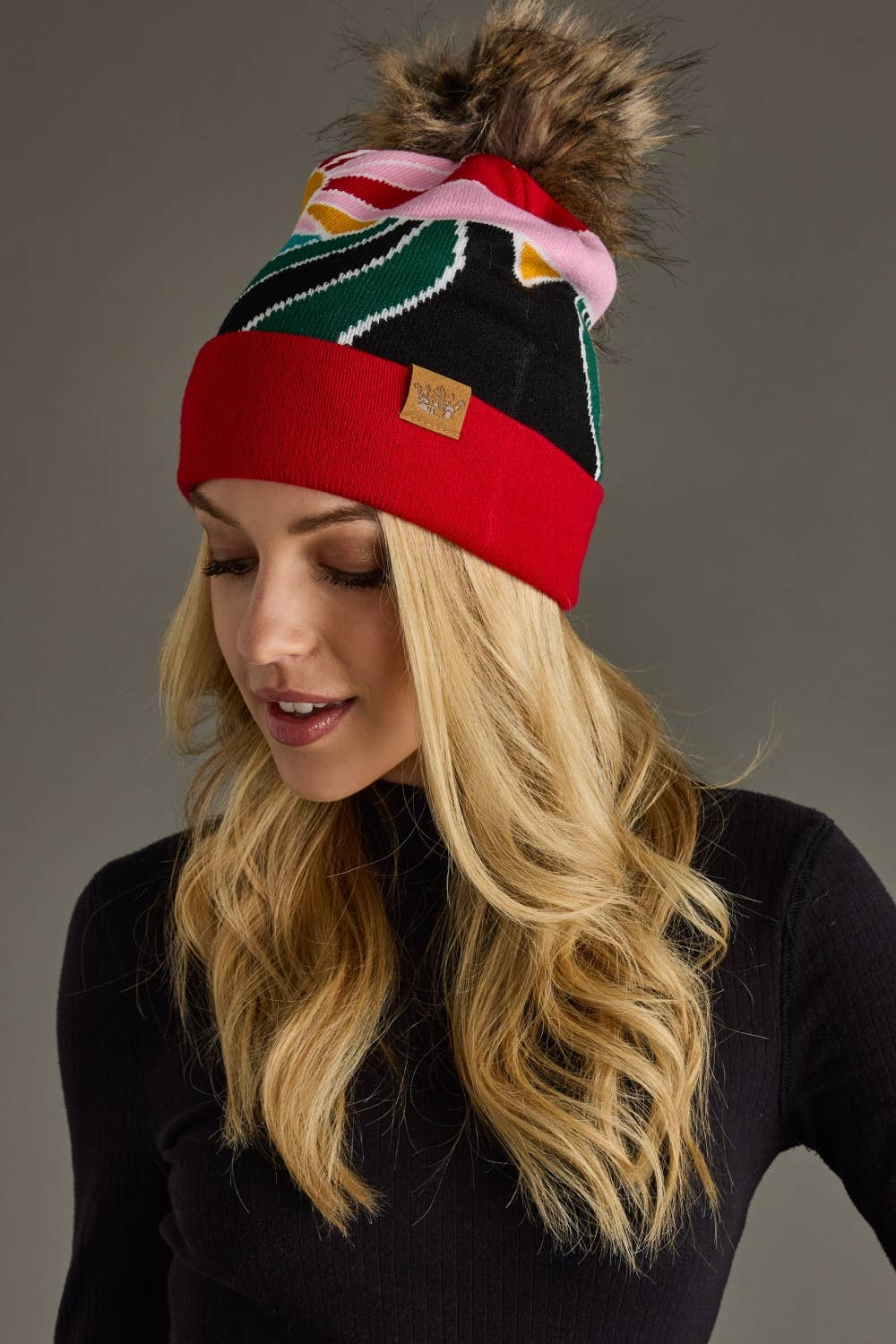 Red & pink sunrise landscape knit hat with natural faux fur pom. Warm, soft, and stretchy blend of 85% acrylic & 15% spandex—cozy winter style with flair.