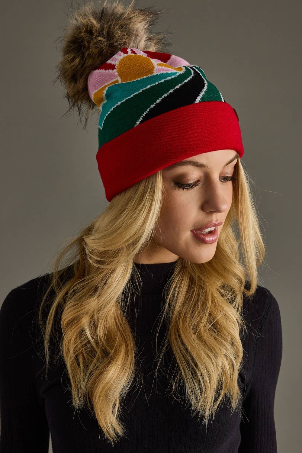 Red & pink sunrise landscape knit hat with natural faux fur pom. Warm, soft, and stretchy blend of 85% acrylic & 15% spandex—cozy winter style with flair.