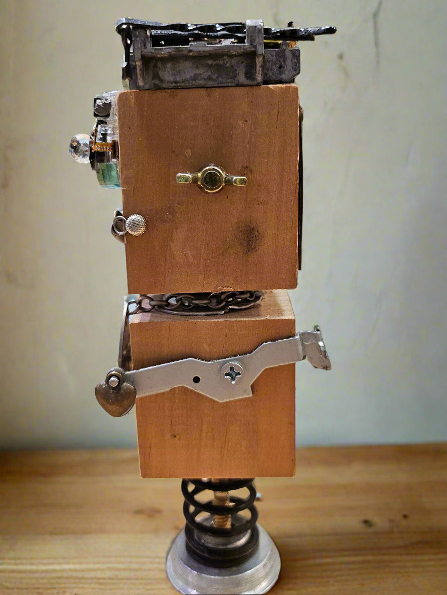 The Handmade Wood Block Steampunk Robot is a unique, decorative figurine crafted from wood with an aged, rustic look. Each robot is one-of-a-kind for display only. Includes a heart-shaped balloon. Available in various sizes, it&