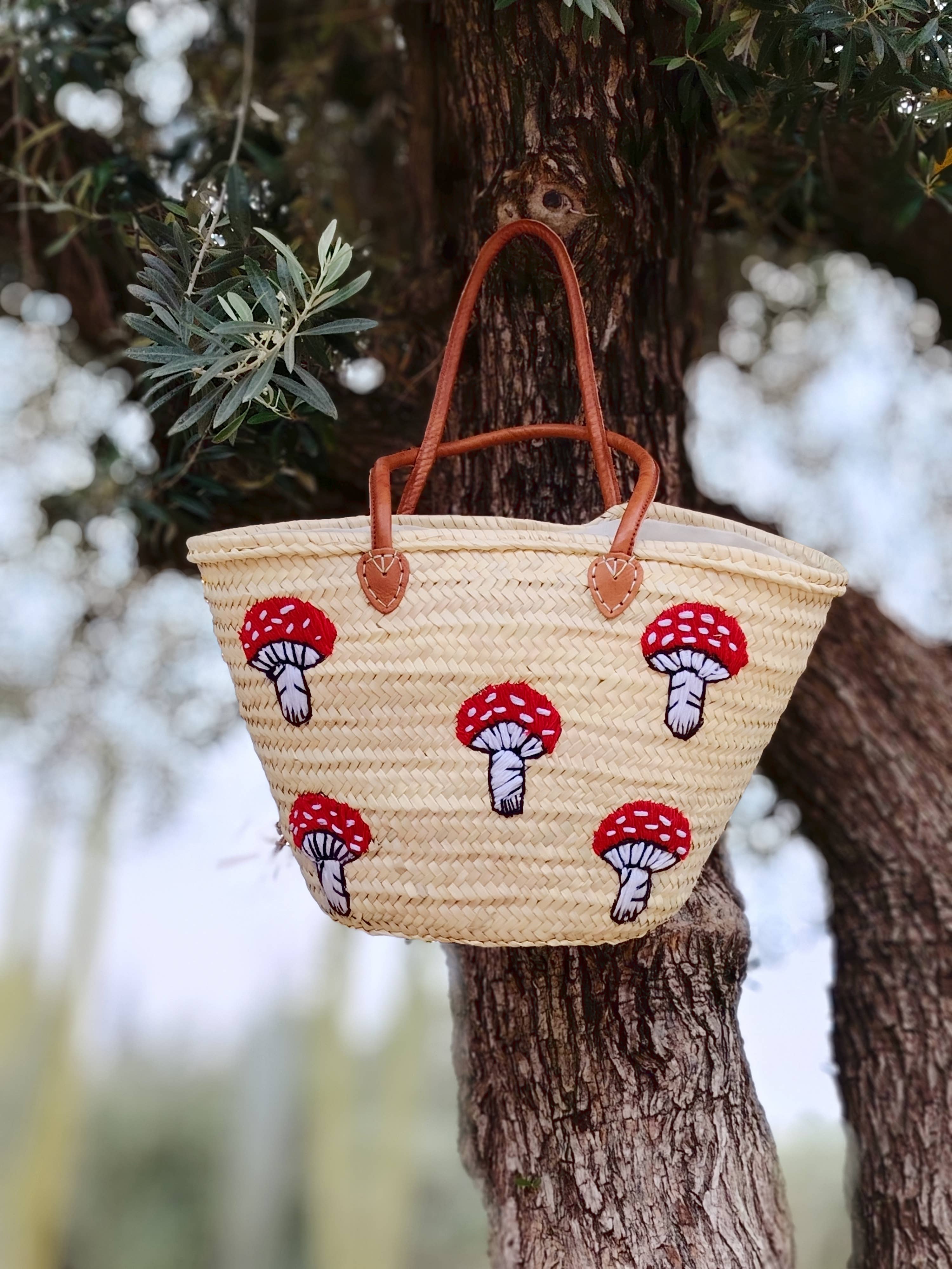 Whimsical straw tote with red mushroom embroidery, leather handles & eco-friendly palm straw. Perfect for market trips, beach days, or unique gifting.