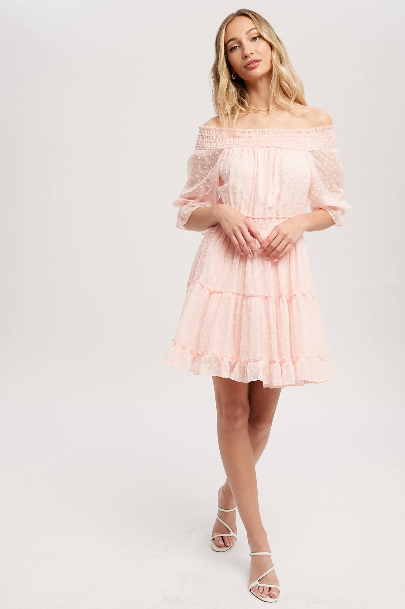Swiss dot chiffon off-the-shoulder mini dress with elastic waist, bell sleeves, and tiered ruffle hem. Soft blush, relaxed fit, feminine silhouette.