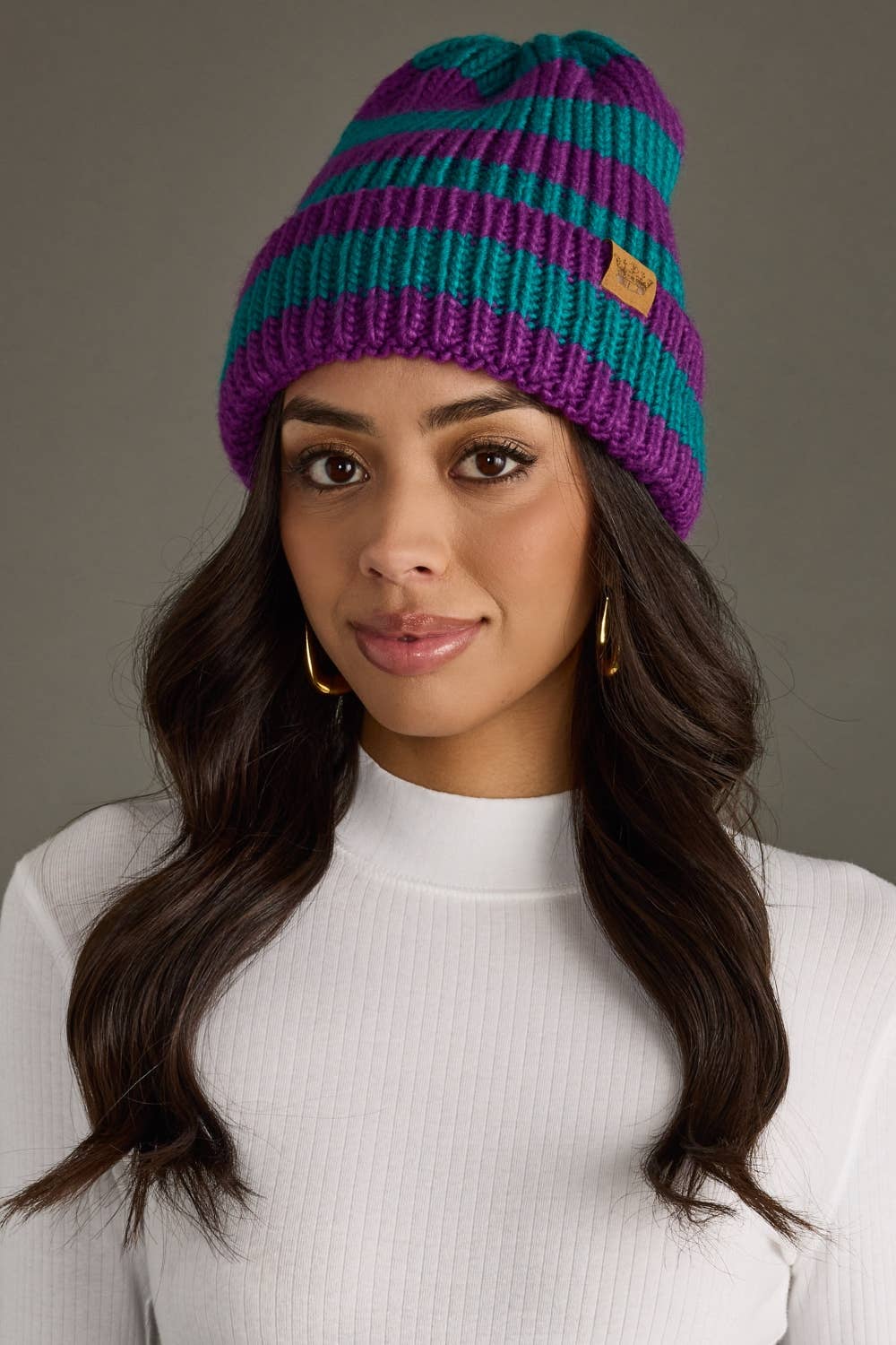 Teal and purple striped chunky knit beanie with a folded cuff and cozy fleece lining. Made from 100% acrylic for warmth and a colorful winter look.