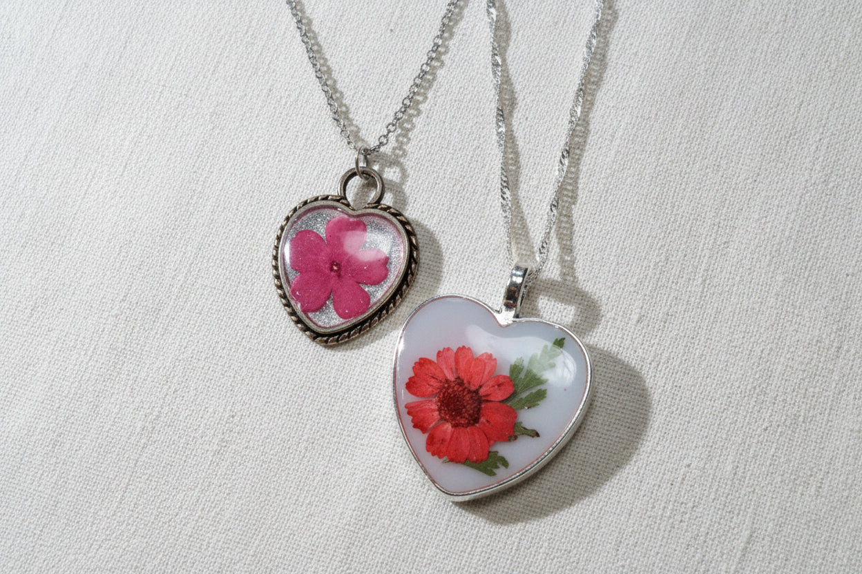 Two romantic floral heart resin necklaces with real flowers preserved in clear resin. Handcrafted, one-of-a-kind botanical jewelry with timeless, sentimental charm.