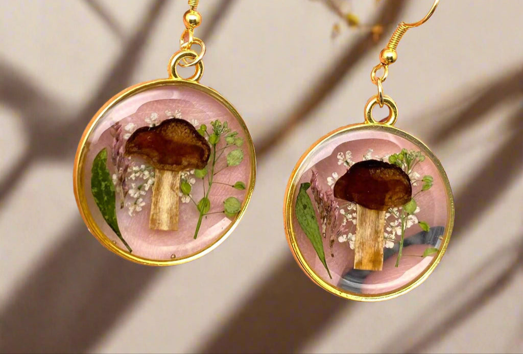 Whimsical dangle earrings with real pressed flowers and tiny mushrooms in resin—each pair is unique and framed in alloy with stainless steel hooks.