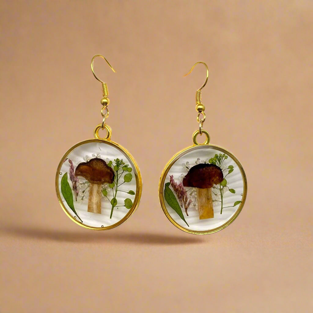 Whimsical dangle earrings with real pressed flowers and tiny mushrooms in resin—each pair is unique and framed in alloy with stainless steel hooks.