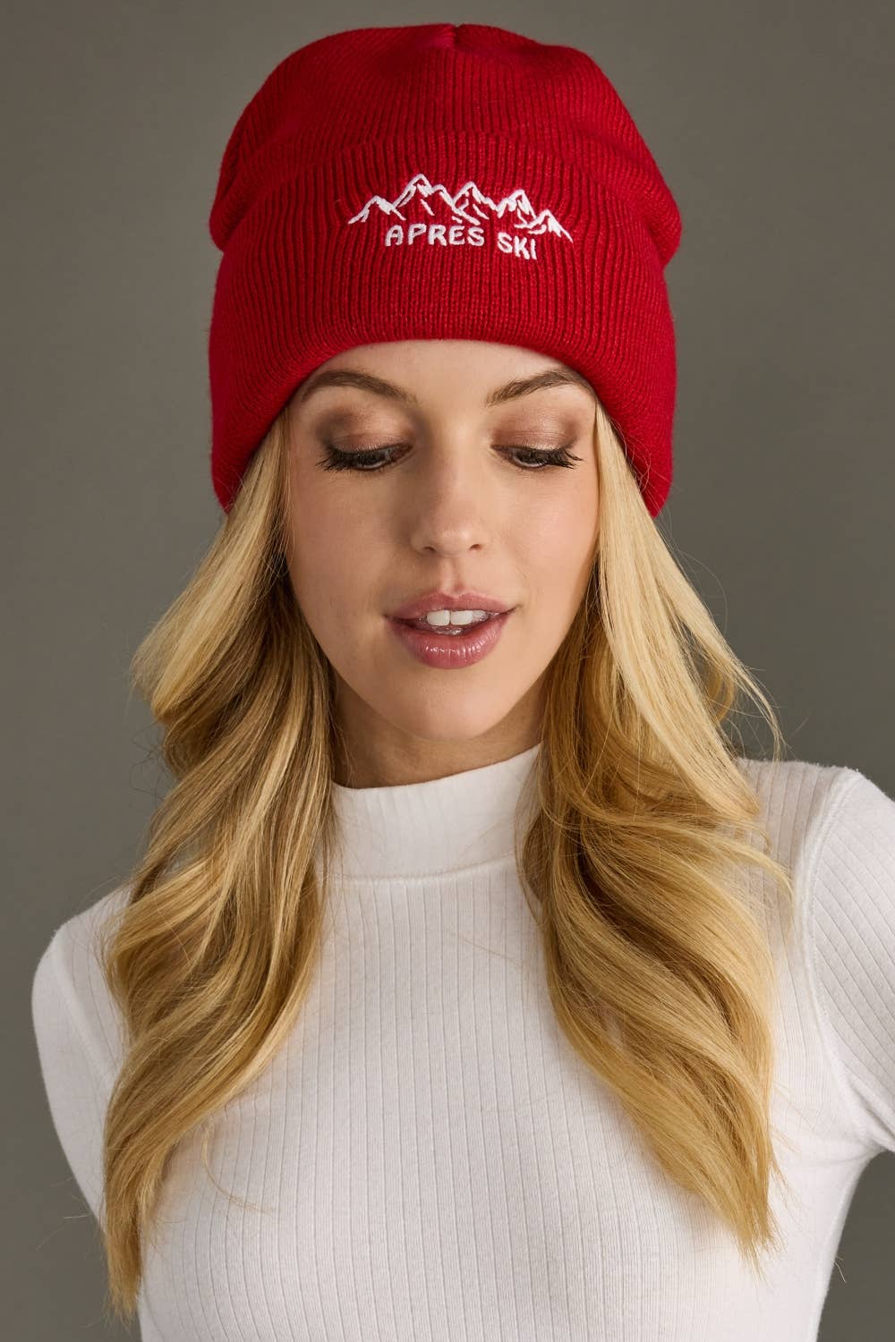 Red knit beanie with white embroidered Apres Ski text and graphic on the cuff. Fleece lined and made from 100% acrylic for cozy, playful winter style.