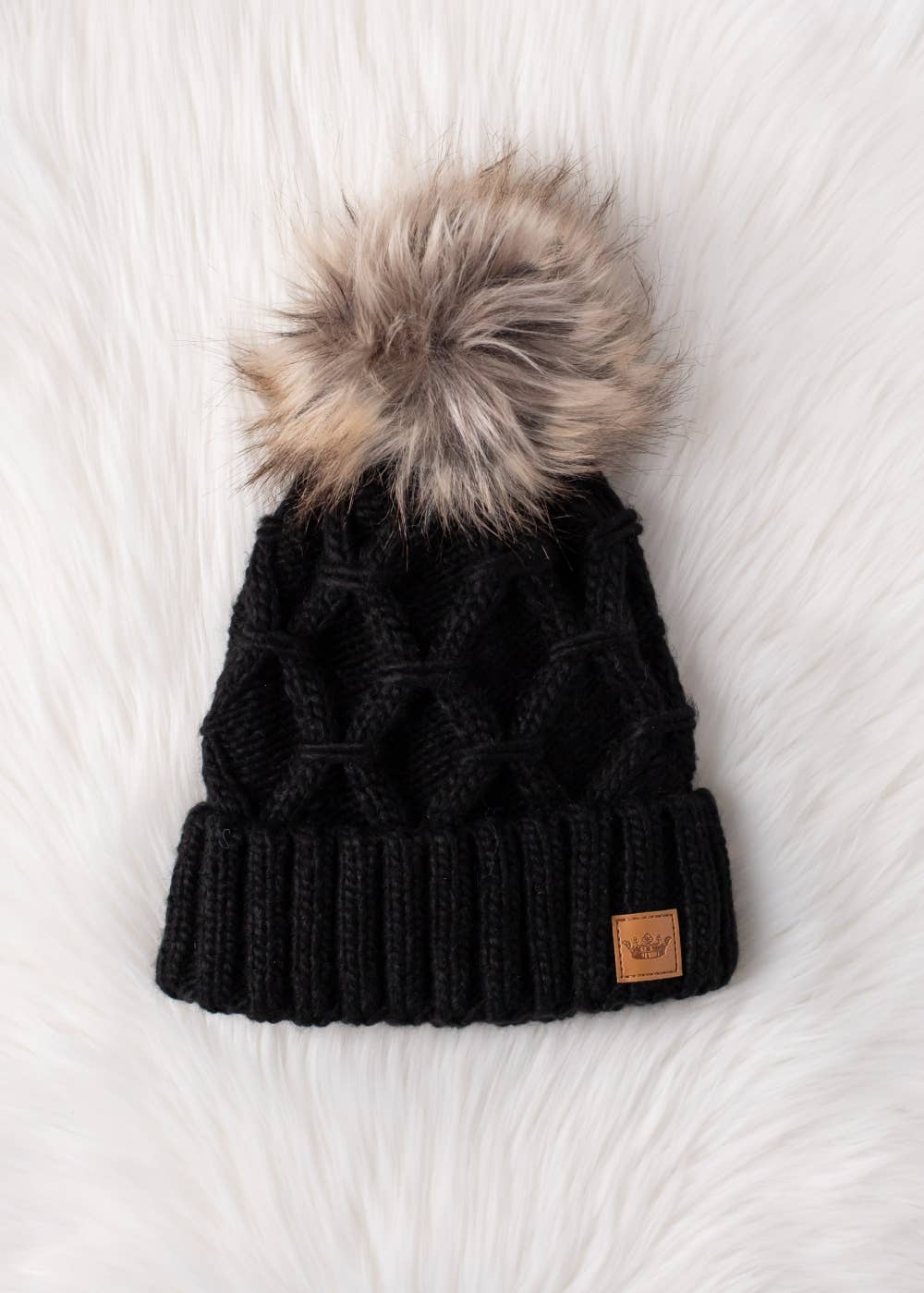 Black diamond cable knit pom hat with natural faux fur pom. Fleece lined for extra warmth and comfort. Classic 100% acrylic design for timeless winter style.
