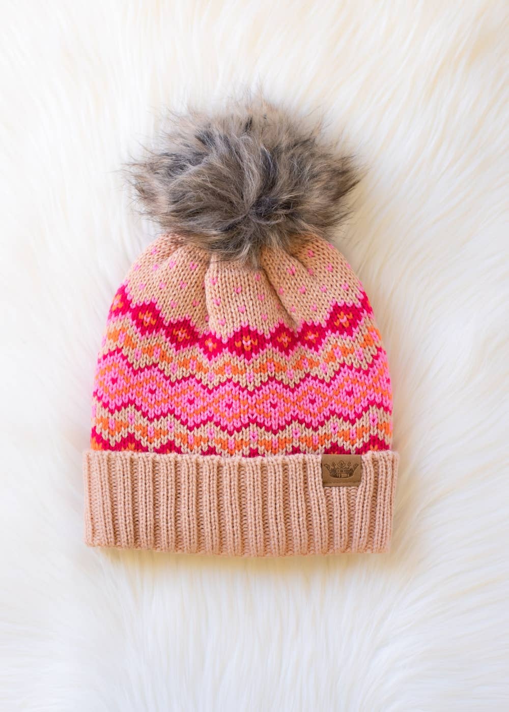 Blush, pink & orange patterned knit hat with natural faux fur pom. Fleece lined for extra warmth & pairs perfectly with matching mittens. 100% acrylic.