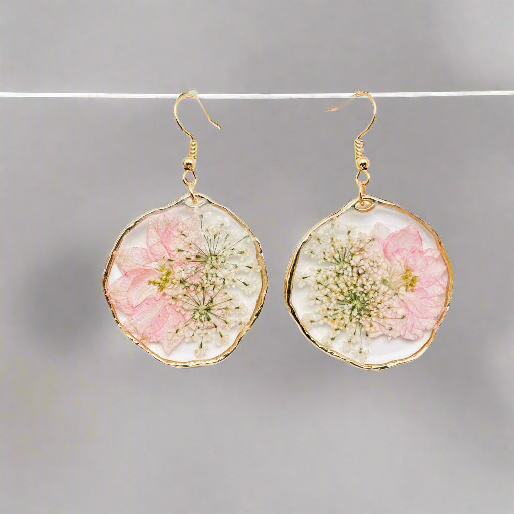 Blushing Bloom earrings feature real pink delphinium and Queen Anne’s Lace in clear resin with copper frames—lightweight, romantic, and naturally one-of-a-kind.